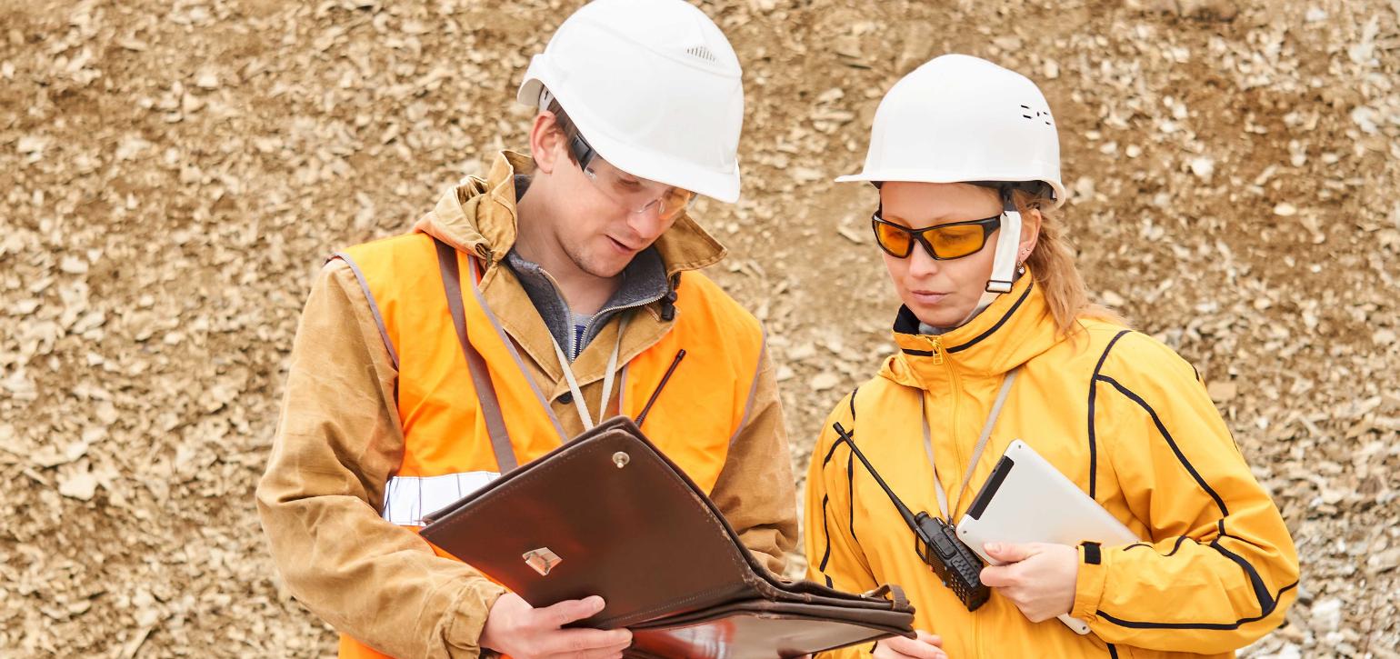 workers in hard hats and protective clothing reading from a folder