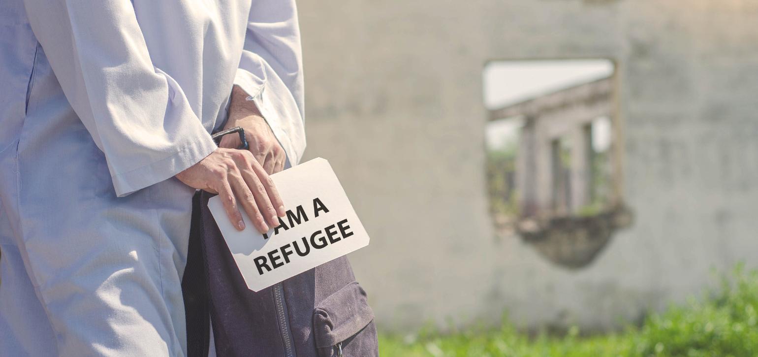 woman with backpack holding sign saying I am a Refugee