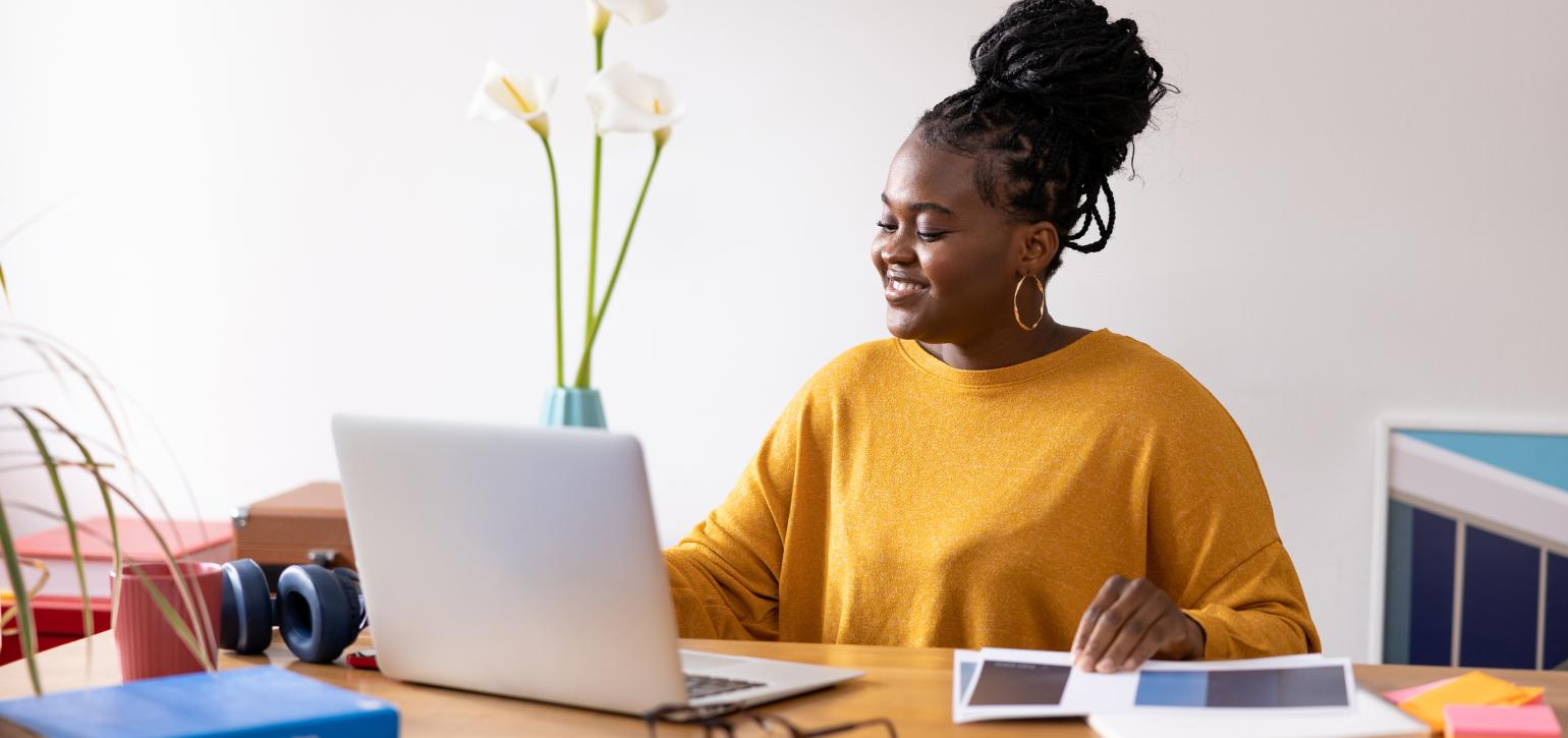 woman in yellow top working at a desk with laptop