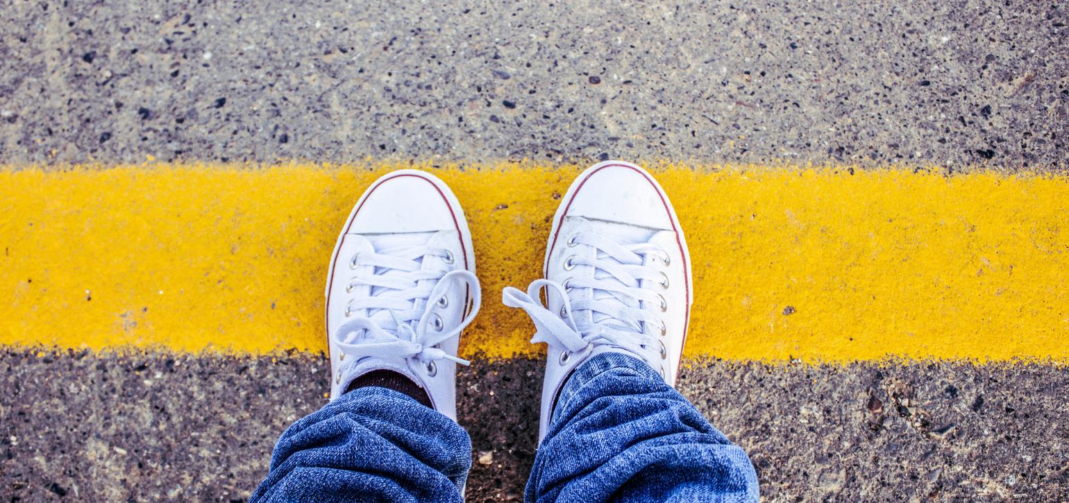 person wearing white sneakers standing at a yellow painted line