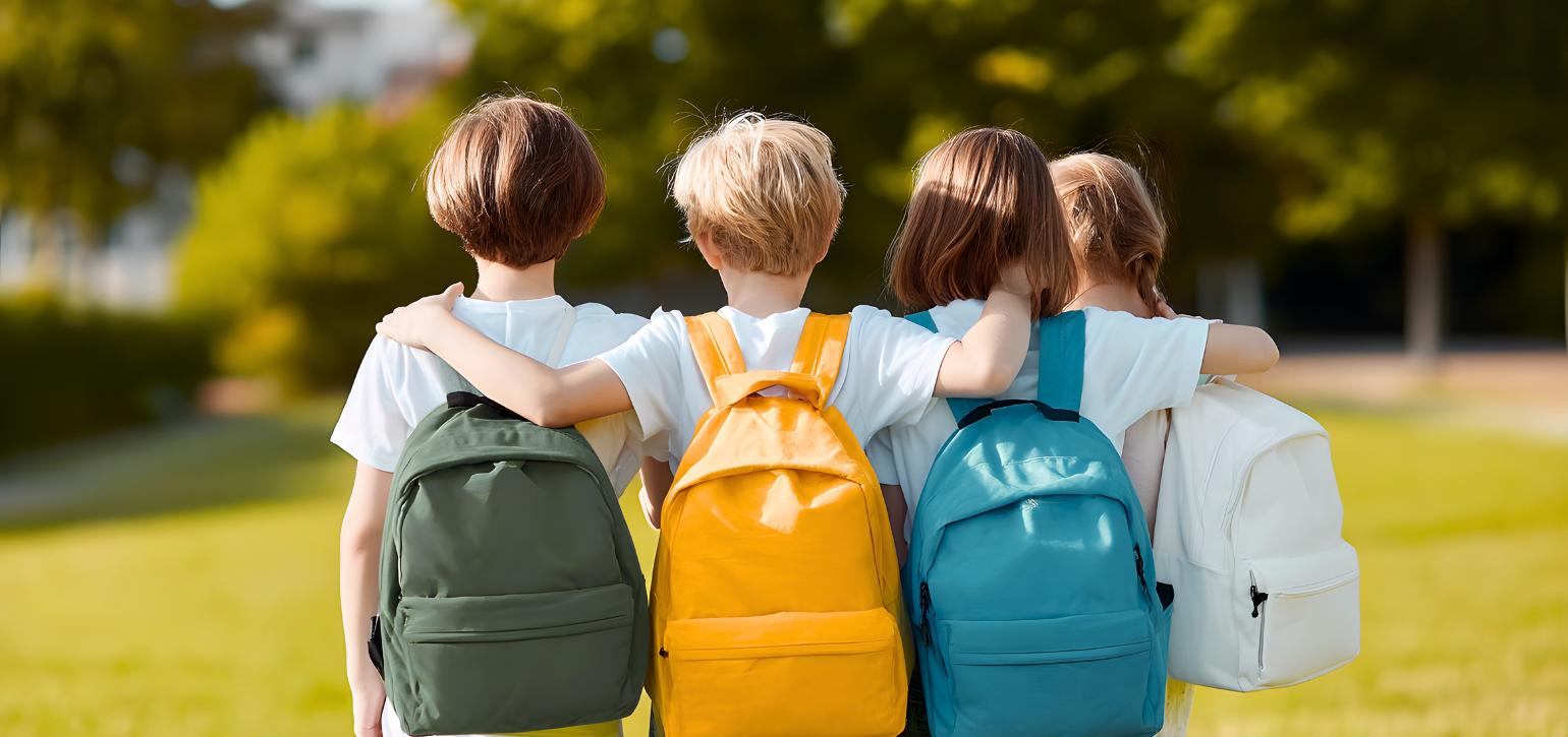 school aged children facing forward in a park with backpacks