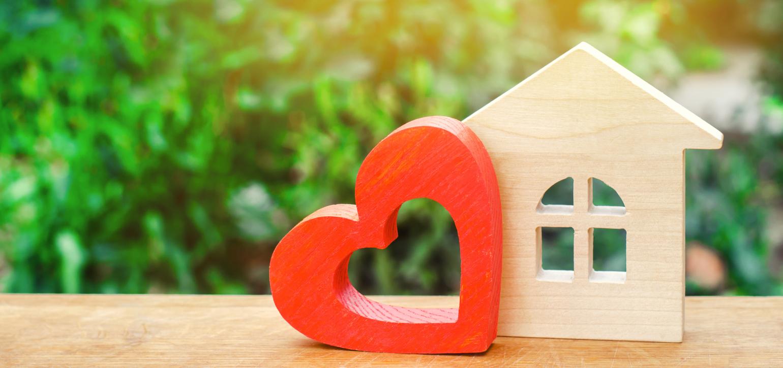 wooden house figurine with red wooden heart figurine on an outdoor table
