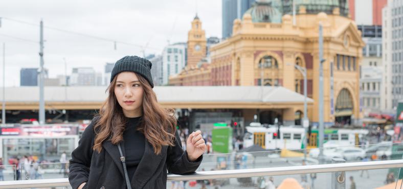 Asian woman standing on bridge in front of Flinders Station